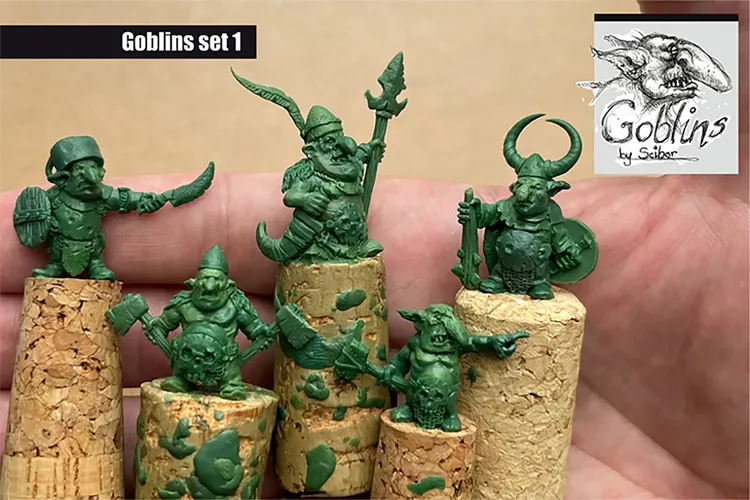 A collection of five green goblin miniatures is displayed, each perched on cork bases. The goblins exhibit distinct features: one wields a sword and shield, another holds an axe, while others sport various weapons and armor, showcasing their mischievous character. The background is neutral, allowing the vibrant green of the miniatures to stand out prominently.