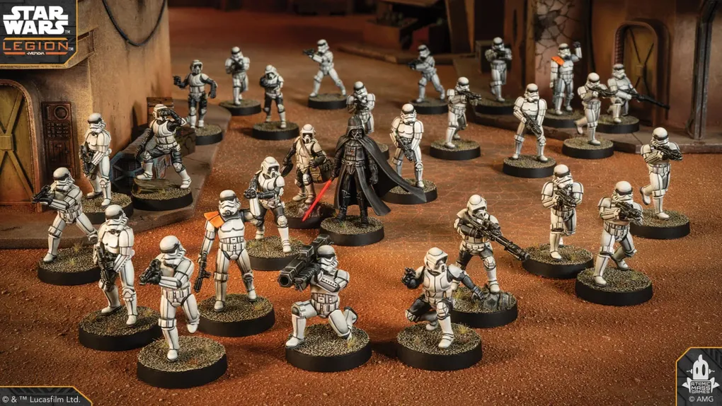 A group of Star Wars miniatures features several Stormtroopers in white armor, positioned in a desert-like environment with a backdrop of a weathered building. Among them stands a prominent figure in black armor, holding a red lightsaber, likely representing Darth Vader. The scene is detailed with various poses of the troopers, some aiming weapons, while others appear to be in action, all set on circular bases with textured surfaces.