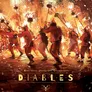 Eight people in red devil costumes with horns and tails, holding flaming maces, dancing on a cobblestone street. Fireworks and sparks surround them. Text at bottom reads "DIABLES" in large gold letters. Credits list "Dani Garcia," "Amelia Sales," and "Dossom Studio" in small text.