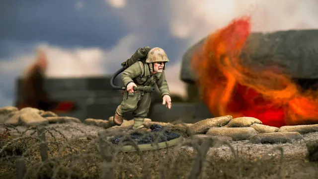 A detailed miniature of a U.S. soldier, Hershel W. 'Woody' Williams, is depicted in action, equipped with a flamethrower on his back and wearing a helmet and military uniform. He is positioned on a textured base that resembles a battlefield, with a backdrop of flames and smoke suggesting a combat environment. The scene captures the intensity of the Pacific theatre during World War II.