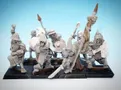 A collection of 28mm scale skeleton warriors from Diehard Miniatures, featuring several figures in various poses. The miniatures are equipped with weapons such as spears and swords, and are adorned with armor and helmets reminiscent of classic Oldhammer designs. The background is a soft blue gradient, highlighting the details of the skeletal figures, which are mounted on black bases.