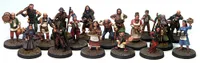 A collection of detailed miniatures representing various fantasy tavern patrons and villagers, arranged in two rows on textured bases. The figures include a mix of characters such as a hooded figure, a woman holding a tray of baked goods, and several others in period-appropriate attire, showcasing a variety of poses and expressions. The overall scene captures the lively atmosphere of a fantasy tavern setting, ideal for tabletop RPGs.