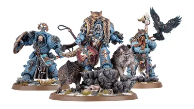 A detailed display features a group of new Space Wolves miniatures, prominently showcasing Logan Grimnar in ornate terminator armor, adorned with a fur cloak and wielding his axe, Morkai. He is flanked by two wolves, Tyrnak and Fenrir, and accompanied by his lieutenants, Arjac Rockfist and Njal Stormcaller, who are also intricately designed. The scene is set on rocky terrain with scattered skulls and grass, enhancing the fierce and wild aesthetic of the Space Wolves.