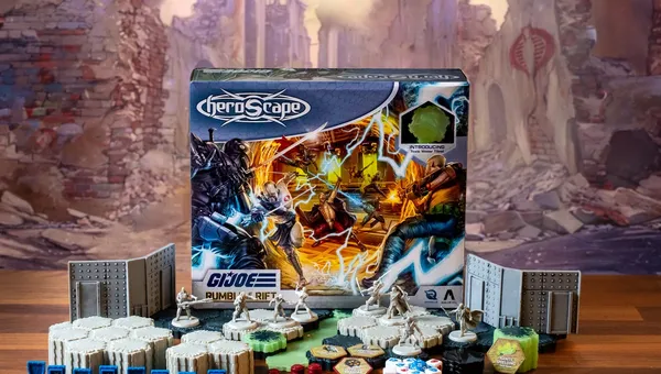A G.I. JOE Heroscape: Rumble at the Rift Battle Box is prominently displayed in the center, featuring vibrant artwork of characters in action. Surrounding the box are various game components, including eight miniatures representing characters like Duke and COBRA Commander, modular hex terrain pieces, COBRA fortifications, dice, and markers. The background features a blurred, crumbling environment, enhancing the game's adventurous theme.