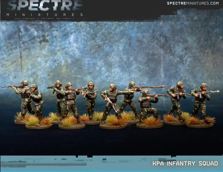 A group of ten miniatures representing a North Korean infantry squad is displayed, featuring soldiers in camouflage uniforms and helmets. They are equipped with Type 88 rifles and RPK-74s, with some holding rifle grenades. The base is adorned with tufts of grass, enhancing the military theme against a textured blue background.