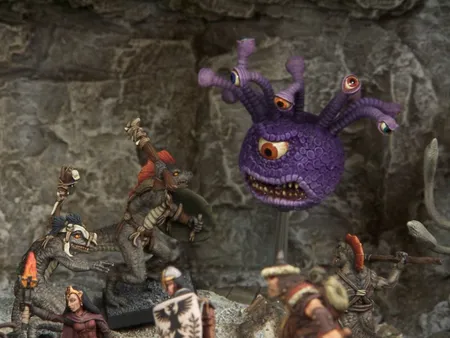 A collection of fantasy miniatures features several lizardmen, one wielding a shield and weapon, and another with a torch, set against a rocky backdrop. In the background, a large, purple creature with multiple eyes and a menacing expression looms, adding to the scene's fantastical atmosphere. A female character in dark robes stands nearby, while other figures in armor are partially visible, enhancing the sense of adventure.