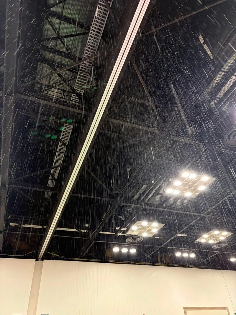 Indoor convention center ceiling with heavy rain leaking through, lights on.