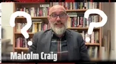 A man with a beard and glasses, dressed in a plaid shirt and blazer, is smiling and gesturing enthusiastically. He is seated in front of a bookshelf filled with various books, suggesting a scholarly environment. The image features large question marks overlaying his face, adding a playful or mysterious element to the scene. The background has a dark, textured border, enhancing the overall dramatic effect.