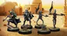 A group of four miniatures from the Star Wars universe is displayed against a desert backdrop featuring a simple structure. On the left, a character in a silver and black armor, resembling a bounty hunter, stands confidently. Next to him, two IG-Series Assassin Droids are posed with weapons drawn, showcasing their metallic bodies and intricate details. In the foreground, Grogu, a small figure with large ears, is depicted holding a small object, adding a whimsical touch to the scene. The ground is textured with grass and dirt, enhancing the overall aesthetic of the miniatures.