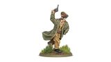 A miniature figure of Lieutenant-General Sir Adrian Carton de Wiart VC is depicted in a dynamic pose, raising a revolver in one hand while wearing a military uniform complete with a long coat and a peaked cap adorned with insignia. The figure stands on a circular base featuring tufts of grass and earthy terrain, emphasizing a battlefield setting. The detailed paintwork highlights his facial features, including a mustache and sunglasses, capturing a spirited and commanding presence.