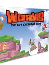 A colorful box for "Worms: The Gift Calendar Game" features a vibrant illustration of cartoonish landscapes with green hills and rocky cliffs. Prominent characters include a pink worm wearing a crown and a knight, both positioned on the cliffs, while a hot air balloon floats in the sky. The title is boldly displayed at the top, emphasizing the festive theme of the advent calendar.