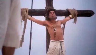 Movie still of crucifixion theme from 'The Life of Brian' where a man is bound to a cross.