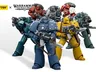 A group of eight tactical space marine action figures stands prominently, showcasing a variety of colors and chapter insignias. The marines are depicted in their original mark of armor, with detailed features and gear, including bolt guns and backpacks. The figures represent popular Warhammer 40k chapters such as the Imperial Fists, Ultramarines, Blood Angels, and Space Wolves, alongside traitorous factions like the Sons of Horus and Alpha Legion.