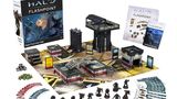 A boxed set for Halo: Flashpoint titled "Feet First into Hell" is prominently displayed, featuring artwork of soldiers in combat. Surrounding the box are 18 detailed miniatures of Orbital Drop Shock Troopers, along with a play mat depicting an urban warzone, several buildings, and various game components including dice, tokens, and cards. The scene is organized, showcasing the miniatures in a dynamic layout, emphasizing the tactical elements of the game.