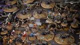 A detailed tabletop scene features various miniatures from the Middle-earth Strategy Battle Game, depicting a tense moment in Mirkwood. Prominent are several large spiders on circular bases, surrounded by a mix of characters including Bilbo, Thorin, and other dwarves, all positioned on a textured terrain with rocks and twisted roots. The dark, earthy colors of the setting enhance the atmosphere of the iconic "Flies and Spiders" chapter from The Hobbit.