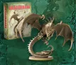 A detailed miniature of an adult dragon is prominently displayed, showcasing its intricate scales, fierce expression, and large, outstretched wings. The dragon is coiled around a rocky base, with its tail elegantly curved. In the background, a box labeled "DRAGONBANE" is visible, indicating the miniature's association with the Dragonbane RPG, set against a textured green backdrop.