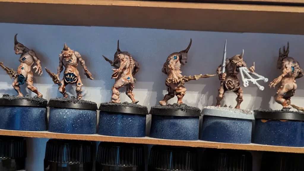 Four miniature figures on round bases, posed in combat stance. Leftmost figure has curved horns, a tusk, and a weapon in one hand. Second figure has a blue gem on its forehead, wielding a club. Third figure holds a large sword and shield. Fourth figure has a multi-pronged weapon.