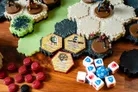 A tabletop gaming scene features modular hex terrain pieces in various colors, including green, gray, and black, arranged on a wooden surface. Prominent elements include several miniatures representing characters from the G.I. JOE universe, along with game components such as red wound markers, white and blue dice, and hexagonal glyph tokens labeled "Jump Pack," "Nanotoxin Coating," and "Glyph of Brandar." The overall setup suggests an engaging battlefield ready for strategic play.
