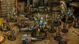 A group of Cygnar miniatures is depicted in a detailed tabletop setting, showcasing the Gravedigger Auxiliaries unit. In the foreground, a character heavy warjack named Beaker stands prominently, adorned in blue and gold armor, with various mechanical features. Surrounding it are several elite veterans, including a female commander with red hair and a rifle, an ogrun captain, and a unit of Gravedigger Commandos, all featuring a mix of blue and gold uniforms, set against a backdrop of stone steps and a weathered door.