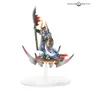A Greater Daemon of Tzeentch miniature on a circular stand. The figure holds a flaming staff in one hand and a curved sword in the other. It wears ornate, colorful armor with intricate patterns in blue, gold, and red. The base has a stylized, wing-like design in pink and purple.