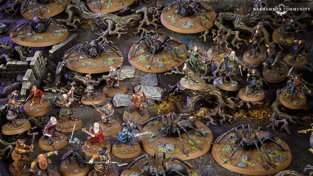 A detailed tabletop scene features various miniatures from the Middle-earth Strategy Battle Game, depicting a tense moment in Mirkwood. Prominent are several large spiders on circular bases, surrounded by a mix of characters including Bilbo, Thorin, and other dwarves, all positioned on a textured terrain with rocks and twisted roots. The dark, earthy colors of the setting enhance the atmosphere of the iconic "Flies and Spiders" chapter from The Hobbit.