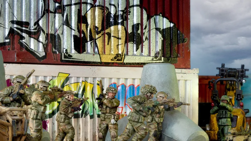Five toy soldiers in camouflage aim rifles behind a graffiti wall.