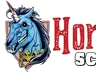 A stylized logo features a blue unicorn with a fierce expression, showcasing sharp teeth and a prominent horn. The unicorn is adorned with a golden collar and is set against a shield-like background. The text "Horror Scotland" is prominently displayed in bold, red letters, with a distressed texture, emphasizing the event's horror theme.