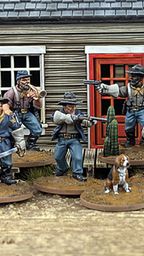 A group of ten detailed 28mm scale miniatures representing dismounted US Cavalry and Buffalo Soldiers stands in front of a wooden building with a red door. The miniatures are posed with various weapons, including rifles and a bugle, showcasing a mix of uniforms and accessories, such as scarves and hats. A small beagle and a cactus are also present among the figures, all mounted on 25mm round bases with a sandy terrain effect.