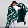 Man in white shirt holding open a green Scrabble-patterned blanket.