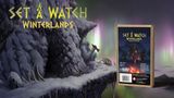A rocky, snow-covered cliffside is depicted, with a mystical aurora borealis illuminating the sky in shades of green and purple. In the foreground, a box for the "Set a Watch: Winterlands" expansion is prominently displayed, featuring dark fantasy artwork that includes shadowy figures and a menacing creature. The title "SET A WATCH WINTERLANDS" is boldly presented at the top, emphasizing the game's theme and expansion details.