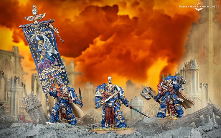 A group of Ultramarines miniatures stands prominently against a dramatic orange and yellow smoky background. Marneus Calgar, the central figure, is adorned in blue armor with gold accents, holding a large banner featuring Ultramarine heraldry. Flanking him are two Victrix Honour Guard, one wielding a sword and the other a weapon, both showcasing intricate details and classic design elements.
