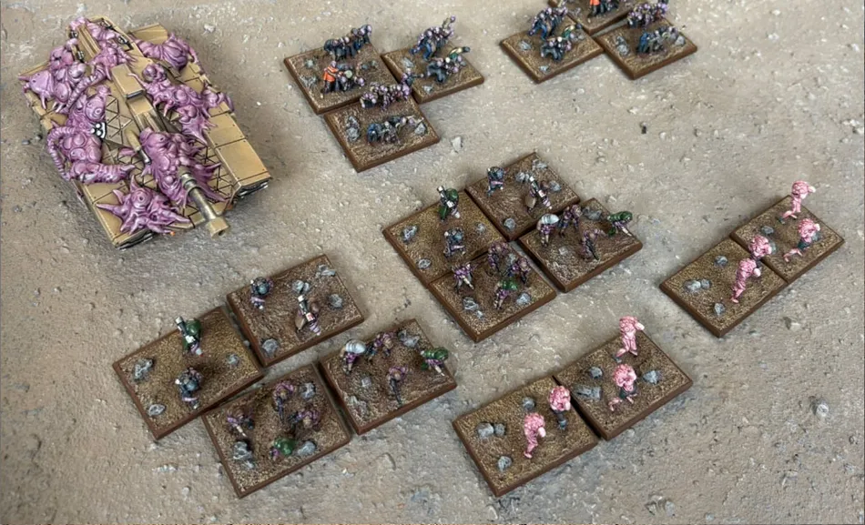 A collection of Zayken miniatures from Void Scar Miniatures is displayed on a textured surface. In the foreground, several bases feature hordes of zombified figures in various colors, including green, purple, and pink, representing the Neophyte Mobs. To the left, a tank is adorned with grotesque, bloated creatures, suggesting a fusion of machine and undead, while additional bases of zombies are scattered throughout the scene, emphasizing the overwhelming numbers of the Zayken forces.