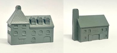 A detailed model of a building designed for 6mm scale wargames, featuring a sloped roof with three dormer windows and a textured surface that resembles slate. The facade includes several arched and rectangular windows, along with a large door at the base, all rendered in a light gray resin. The overall design suggests an industrial style, suitable for various historical or modern warfare settings.