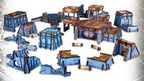 A collection of tabletop gaming terrain pieces in a futuristic style, featuring various structures such as buildings, platforms, and ruins. The pieces are predominantly blue with brown accents, showcasing intricate details and textures. Some structures are elevated, while others are flat, creating a diverse landscape suitable for gaming scenarios.