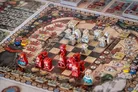 Board game with chess pieces, red and white figures, and illustrated fantasy-themed board.