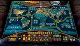 A detailed game board for "Earth Siege: Arrival" features a world map divided into regions, including North America, South America, Africa, Europe, Asia, and Oceania, with various icons representing military and political elements. The board includes a turn track and combat track at the bottom, along with indicators for human base defense and resources. Bright colors and a futuristic design enhance the thematic elements of an alien invasion scenario.