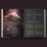A visually striking open book features the chapter titled "The Fractured Library," with elegant gold lettering on a dark background. The left page displays a dramatic image of a fragmented space station, surrounded by swirling cosmic elements, while the right page contains text detailing the chapter's background and narrative. The overall aesthetic combines a sense of mystery and adventure, fitting for a science fiction roleplaying game.