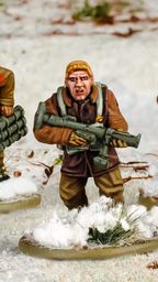 Three multi-part British and Canadian winter infantry figures are depicted in a snowy landscape. The central figure, with short blond hair, is holding a rifle and wearing a brown coat, while the other two figures are dressed in winter gear, one carrying a set of explosives and the other holding a sidearm. The bases of the figures are adorned with patches of snow and tufts of grass, enhancing the wintery scene.