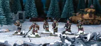 A group of six multi-part British and Canadian winter infantry figures stands on a snowy terrain, surrounded by evergreen trees and a tank in the background. Each figure is dressed in warm winter gear, showcasing a variety of poses and equipped with different weapons, including rifles and sidearms. The scene captures the essence of a winter battlefield, with patches of snow and scattered debris enhancing the atmosphere.