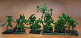 A collection of old school miniatures from Satyr Art Studio, featuring various fantastical creatures in a vibrant green color. The figures include beastmen with distinct features such as horns and claws, some wielding weapons, and a central figure holding a staff topped with a skull and a crescent. They are displayed on black bases against a warm, textured background.