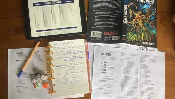 Topdown photo of a solo game in progress. Roll table from Mythic on tablet, Monster of the Week rulebook, journal for note taking, reference sheets
