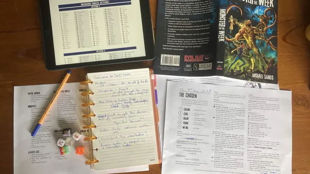 Topdown photo of a solo game in progress. Roll table from Mythic on tablet, Monster of the Week rulebook, journal for note taking, reference sheets
