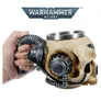 A hand holds a detailed model of a servo skull from the *Warhammer 40,000* universe. The skull is beige with mechanical components attached, including a metallic cylindrical cup embedded in the top of its cranium. A flexible, coiled cable extends from the back of the skull, wrapped around the hand’s fingers. On the side of the skull, near the temple, is a small black Imperial Aquila symbol. Above the image, a metallic banner displays the text: "WARHAMMER 40,000" in bold, silver letters.