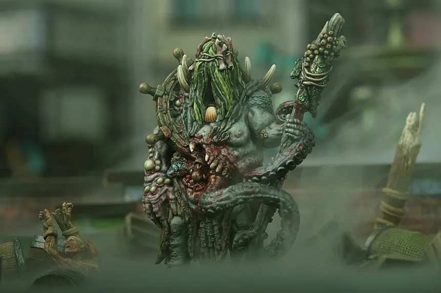 Green-skinned monster with long hair, horns, and a staff, holding a severed head.