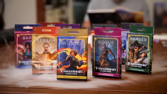 Four colorful Class Packs for the Daggerheart tabletop roleplaying game are displayed prominently. The packs are labeled "BARBARIAN," "SERAPH," and "WIZARD," each featuring unique artwork representing the respective classes. The background includes a soft, smoky effect, enhancing the fantasy theme of the scene.