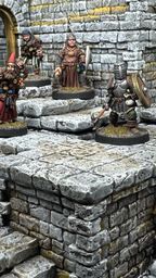 A detailed scene showcases a modular dungeon setup made from intricately sculpted stone blocks, featuring various levels and staircases. Four miniatures are positioned on the blocks: a bearded wizard with a staff, a robed figure holding a spear, and a knight in armor wielding a weapon, all engaged in exploration. The textured stone surfaces and the overall layout highlight the versatility of the dungeon blocks for tabletop gaming.