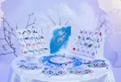 Boardgame components on a white table: Arctic wildlife cards showing fish, seals, whales, and birds; a circular game board with a blue Arctic map; hexagonal tiles with animal icons; and small circular tokens in blue, green, and purple. Central artwork depicts a blue whale.