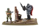 A detailed miniature scene features a soldier in military attire, holding a futuristic weapon, standing beside a crumbling brick wall. Opposite him, a heavily armored mech with a prominent red cape stands confidently, brandishing a spear-like weapon. The base is textured with grass and rocks, enhancing the dynamic and gritty atmosphere of the setting.