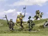 A group of halfling miniatures stands on a grassy terrain, showcasing their unique characteristics. In the center, a halfling in ornate armor rides a large, lion-like creature, holding a blue and white banner. To the left, another halfling wields a spear, while a third, dressed in green, brandishes a hammer. A fourth halfling rides a smaller, dog-like creature, completing the ensemble of pint-sized warriors. The background features a soft blue sky with scattered clouds, enhancing the whimsical atmosphere.