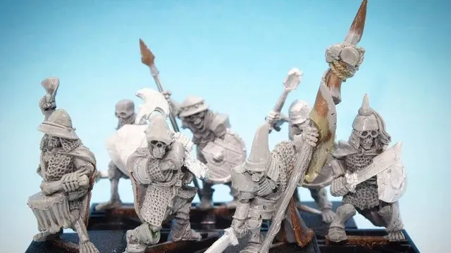 A collection of 28mm scale skeleton warriors from Diehard Miniatures, featuring several figures in various poses. The miniatures are equipped with weapons such as spears and swords, and are adorned with armor and helmets reminiscent of classic Oldhammer designs. The background is a soft blue gradient, highlighting the details of the skeletal figures, which are mounted on black bases.